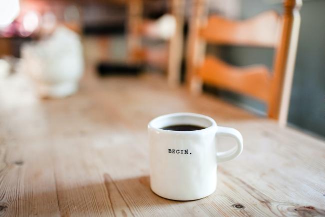 På ett bord står en kaffekopp med texten Begin